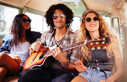 two women in sunglasses sitting in a van next to a man playing guitar